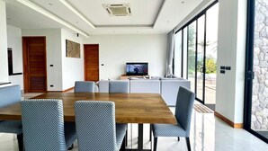 A modern dining area with a wooden table and patterned chairs, a ceiling fan, and a television in the background. - Michel Tropical Seaview Pool Villas  (Mae Nam)