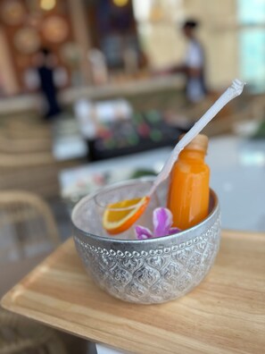 Un tazón de vidrio con un diseño decorativo, conteniendo una bebida con pajita y una rodaja de naranja, sobre una mesa de madera.