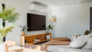 Una sala de estar moderna con un sofá, una mesa de centro, un televisor montado en la pared, una lámpara y una estantería.