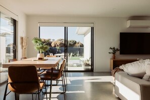 Una sala de estar moderna con comedor, puertas correderas de vidrio que dan a un patio trasero, un televisor de pantalla plana y un sofá cómodo.