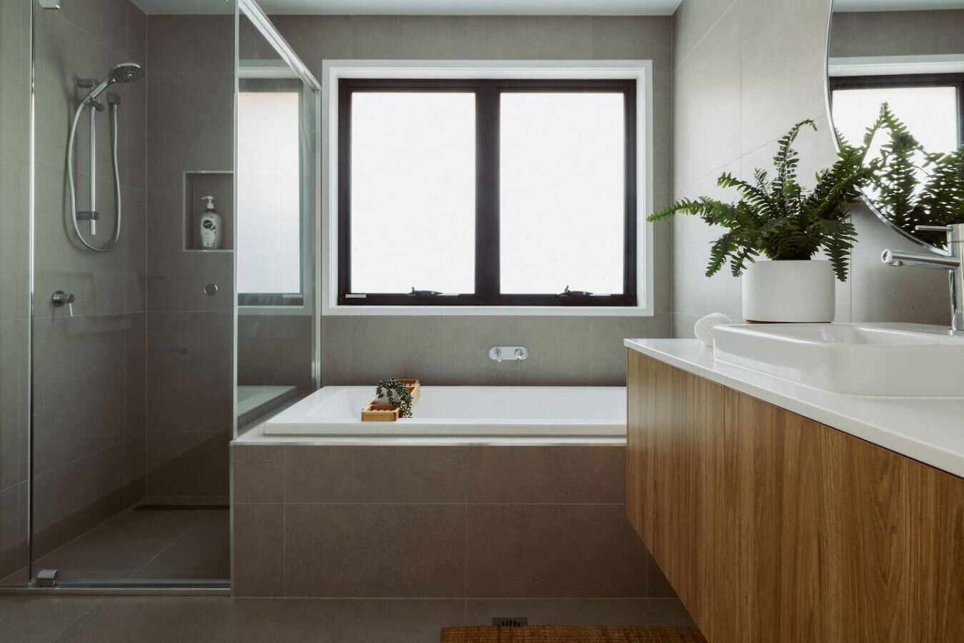 A modern bathroom with a bathtub, a shower, a window, and a potted plant.