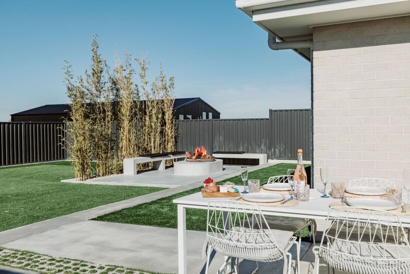 Un patio trasero con una fogata, mesa de comedor exterior y sillas.