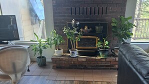 A living room with a fireplace, wooden flooring, a black leather sofa, and potted plants. -    Cozy cottage for vacation in Cedar Ridge near its famous trail. (Sonora)
