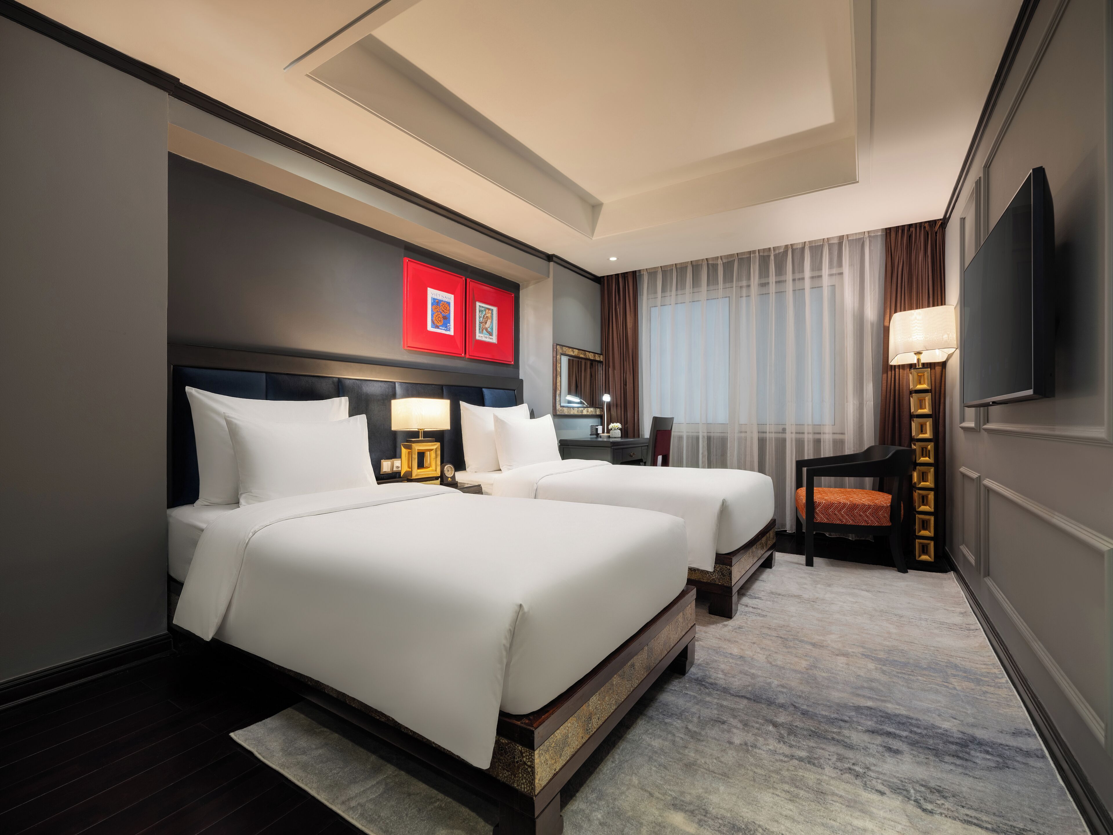 A hotel room with two beds, a desk, a chair, a TV, and a window with curtains.