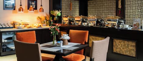 Restaurante com buffet, incluindo mesa com cadeiras e um vaso de flores.