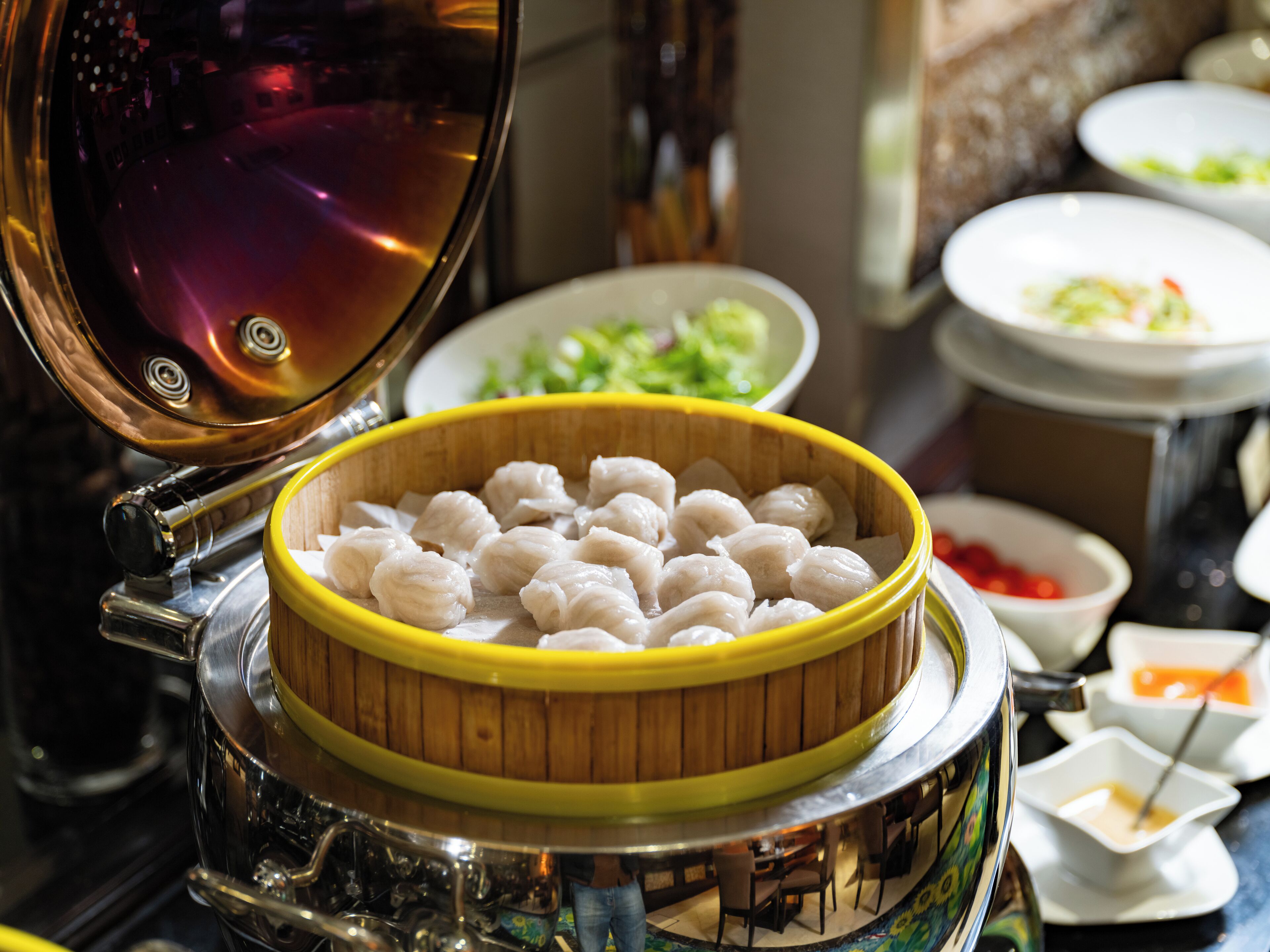 A steamer with dumplings and various dishes in the background.
