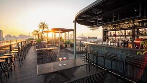 A rooftop bar with outdoor seating, a bar counter, and a city skyline view.
