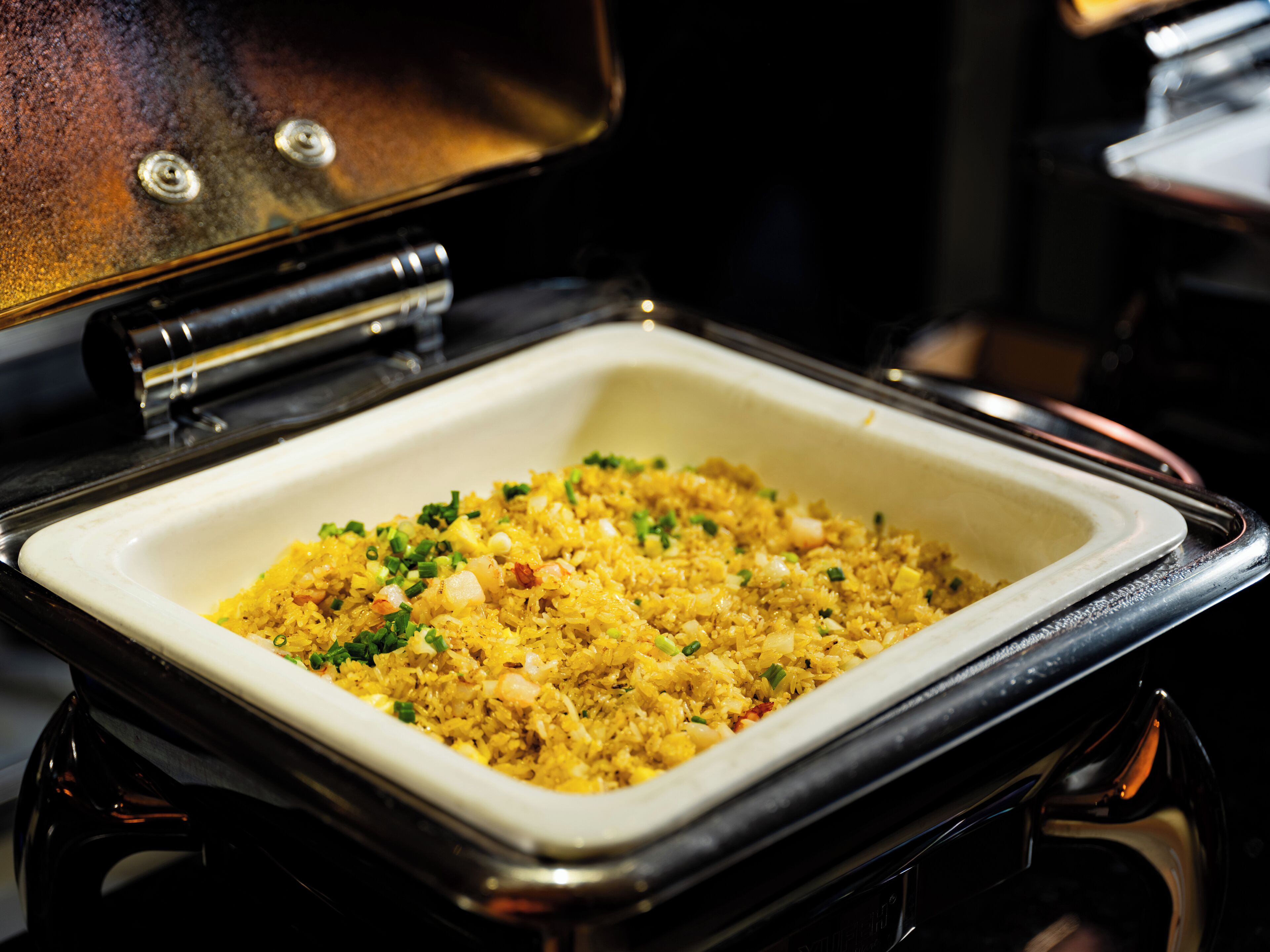 Un recipiente rectangular blanco lleno de arroz amarillo adornado con cebollines, sobre una estufa negra.