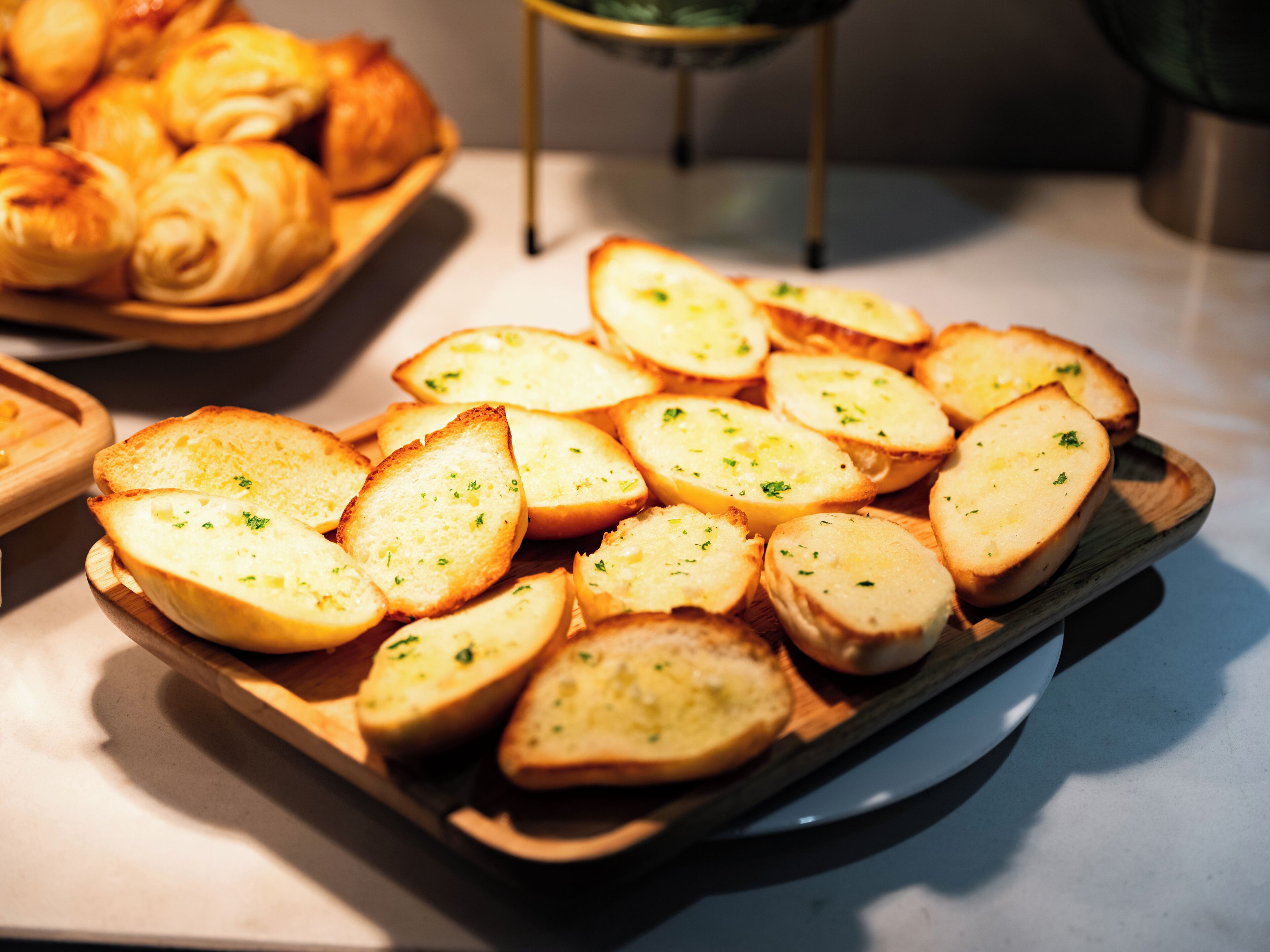 A wooden serving tray with sliced bread garnished with herbs, placed on a countertop.