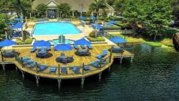 A pool area with a wooden deck, lounge chairs, and umbrellas. - Modern 3BR Retreat with Comfort & Style Near Disney (Kissimmee)
