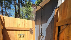 Ein Duschbereich im Freien aus Holz mit einer Metallrost-Fußbodenfläche, umgeben von Holzvertäfelungen und einem Holzzaun.