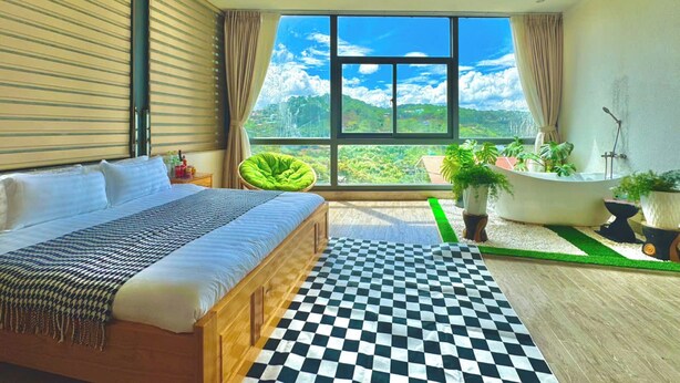 Un dormitorio con una cama grande, suelo a cuadros, vistas a montañas, una silla verde y una bañera.