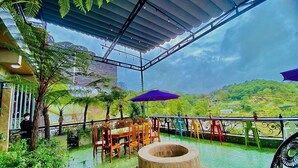 Un patio al aire libre con un pozo de fuego redondo, mesas y sillas de madera, y sombrillas.