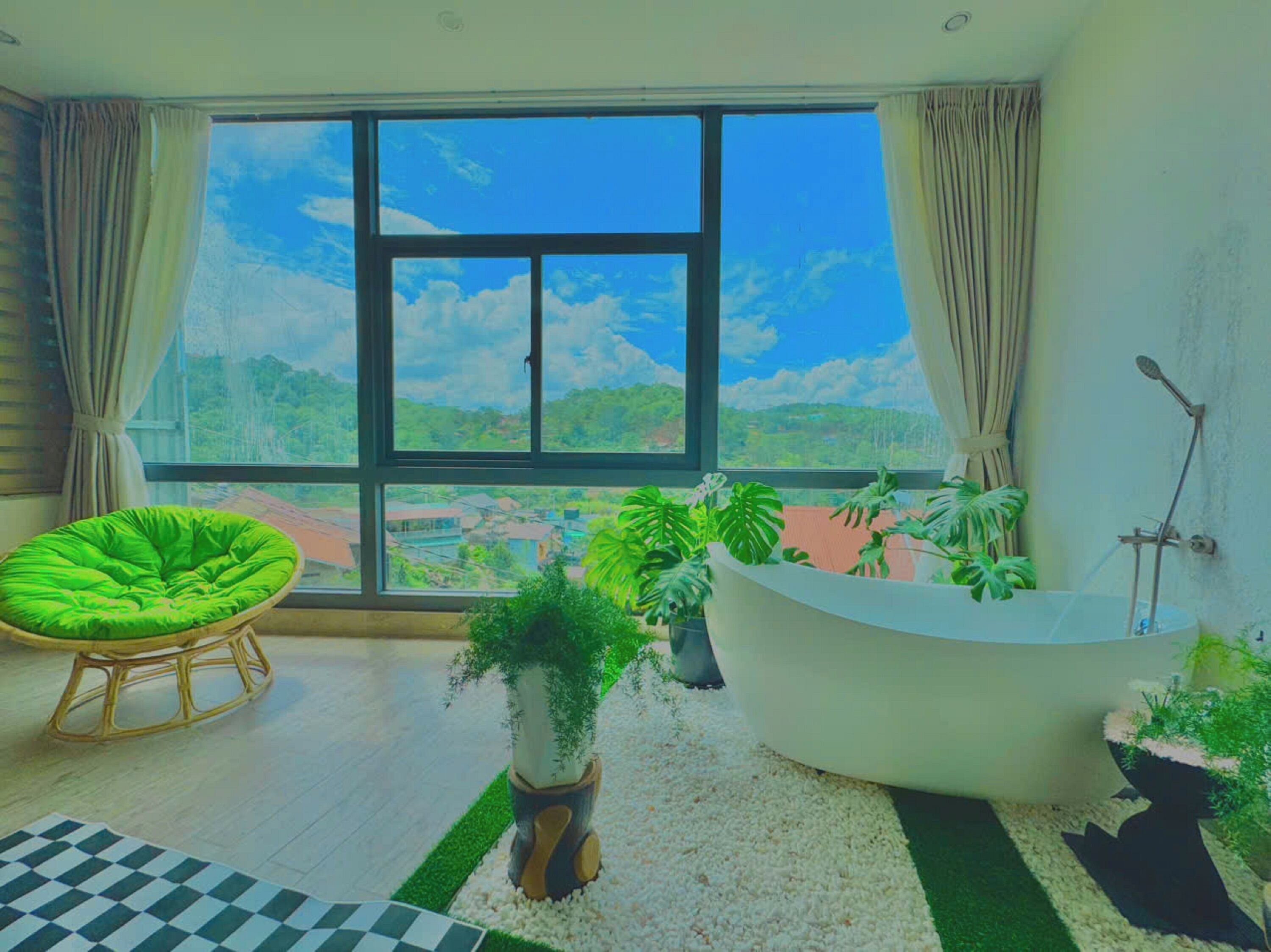Una habitación amplia con un ventanal grande, una silla verde, una bañera y varias plantas en macetas.