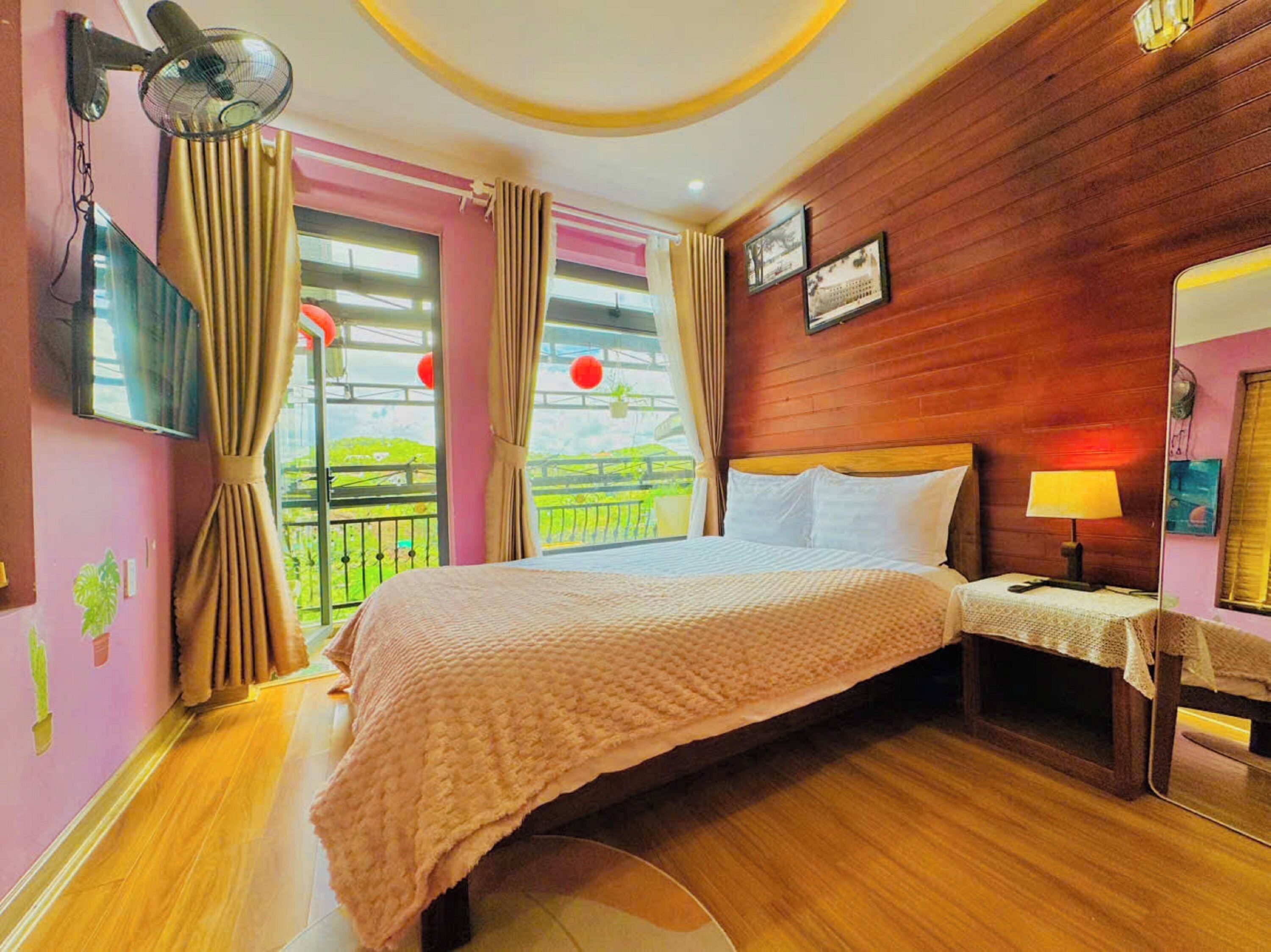 A hotel room with a bed, a nightstand, a lamp, and a view of a balcony with red lanterns.