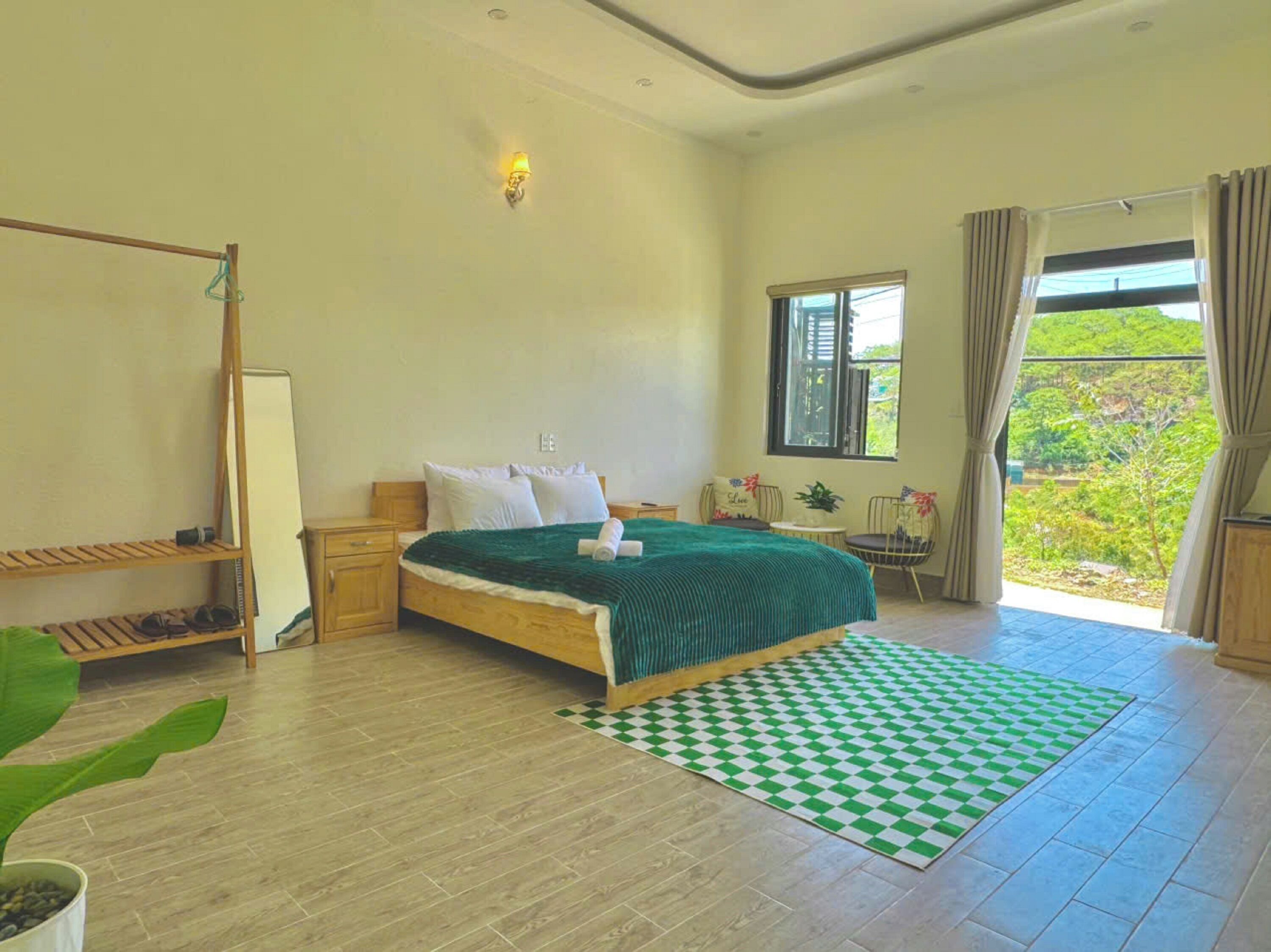 Un dormitorio con cama, ventana, vistas a zonas verdes, suelo de madera y alfombra a cuadros.