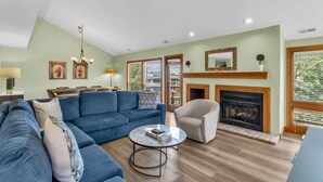 A modern living room with a blue sofa, a round coffee table, a fireplace, and a dining area with a table and chairs.