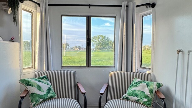 Una habitación con dos sillas a rayas, un tapete estampado y vista a un campo verde a través de una ventana.