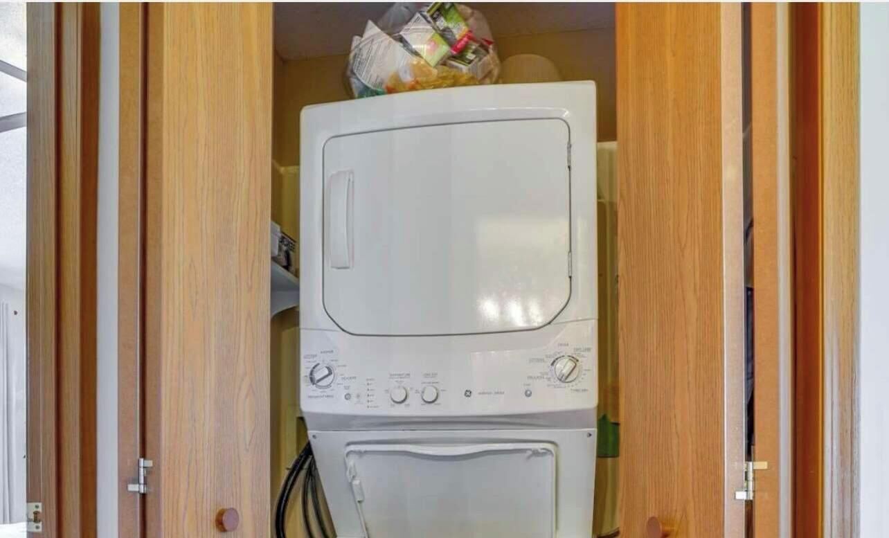Habitación pequeña con lavadora y secadora, puertas de madera y un cable eléctrico a la vista.