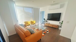 Ett modernt vardagsrum med en soffa i läder, gula stolar, ett soffbord i glas och en tv med platt skärm.