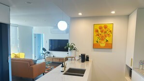 Ett modernt kök med en köksö i mitten, en platt-TV och en tavla med blommotiv på väggen.
