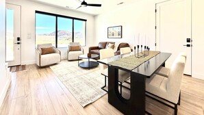 Un salon moderne doté d’une grande fenêtre, d’un ventilateur de plafond et d’un coin repas avec une table et des chaises.