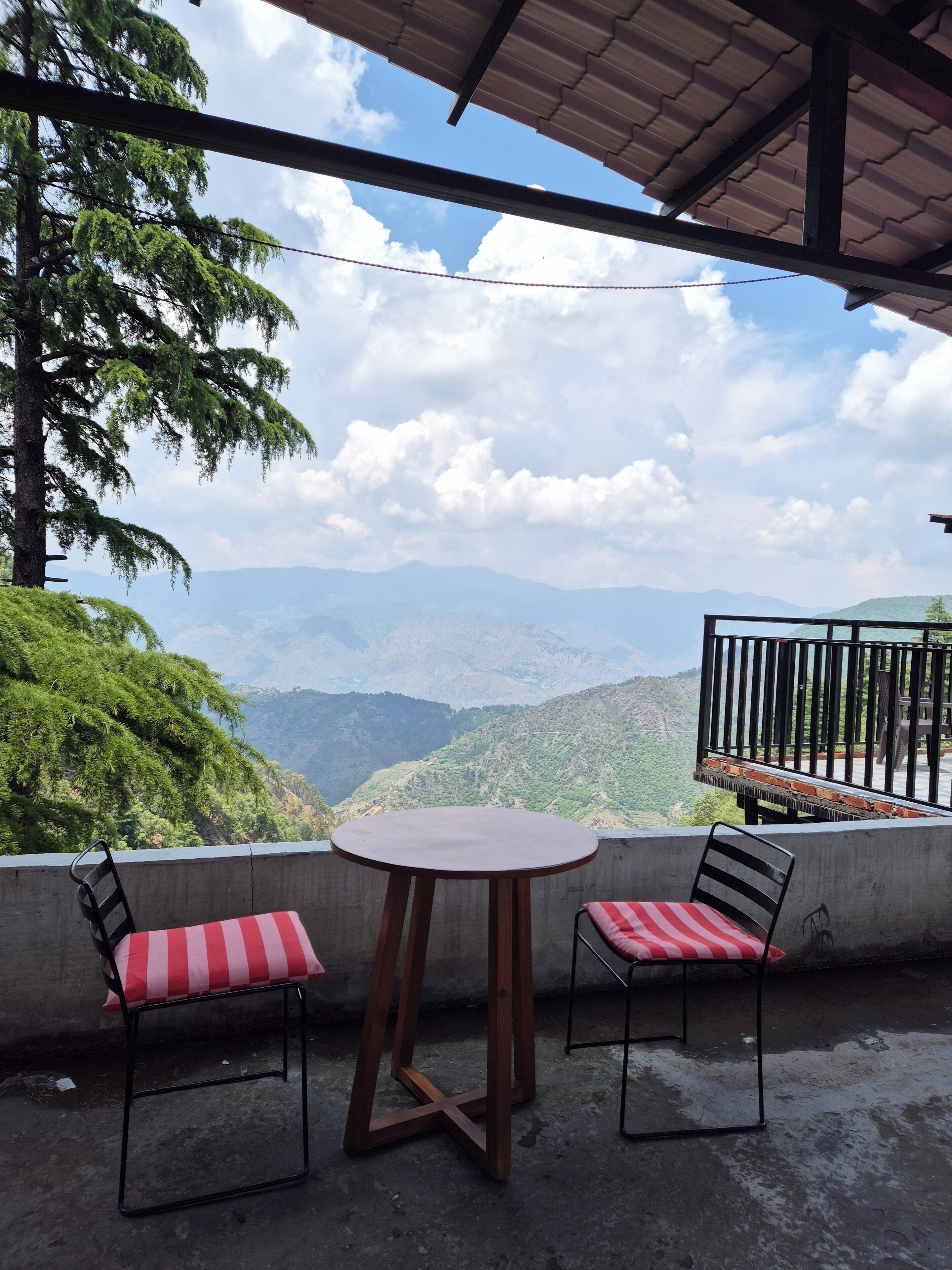 A terrace with a round table and two chairs, overlooking a mountainous landscape.