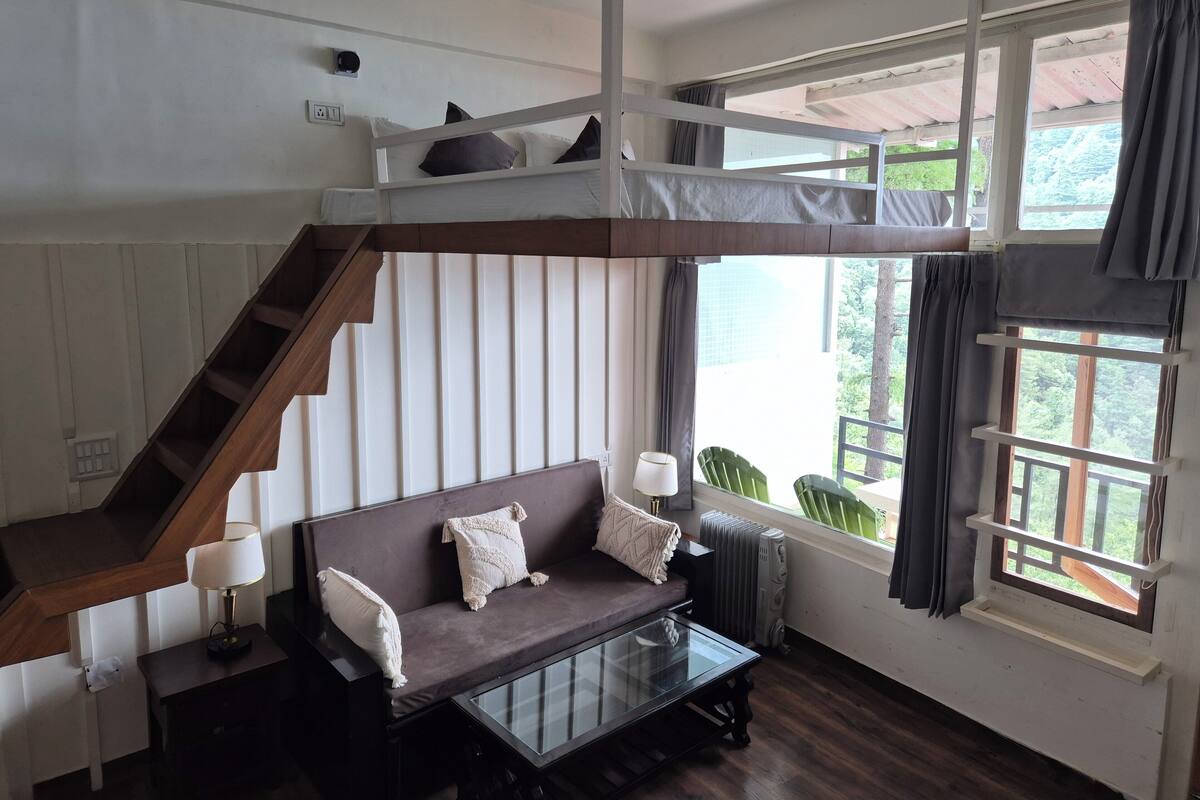 Een kamer met een stapelbed, een slaapbank, een glazen salontafel en uitzicht op groen.