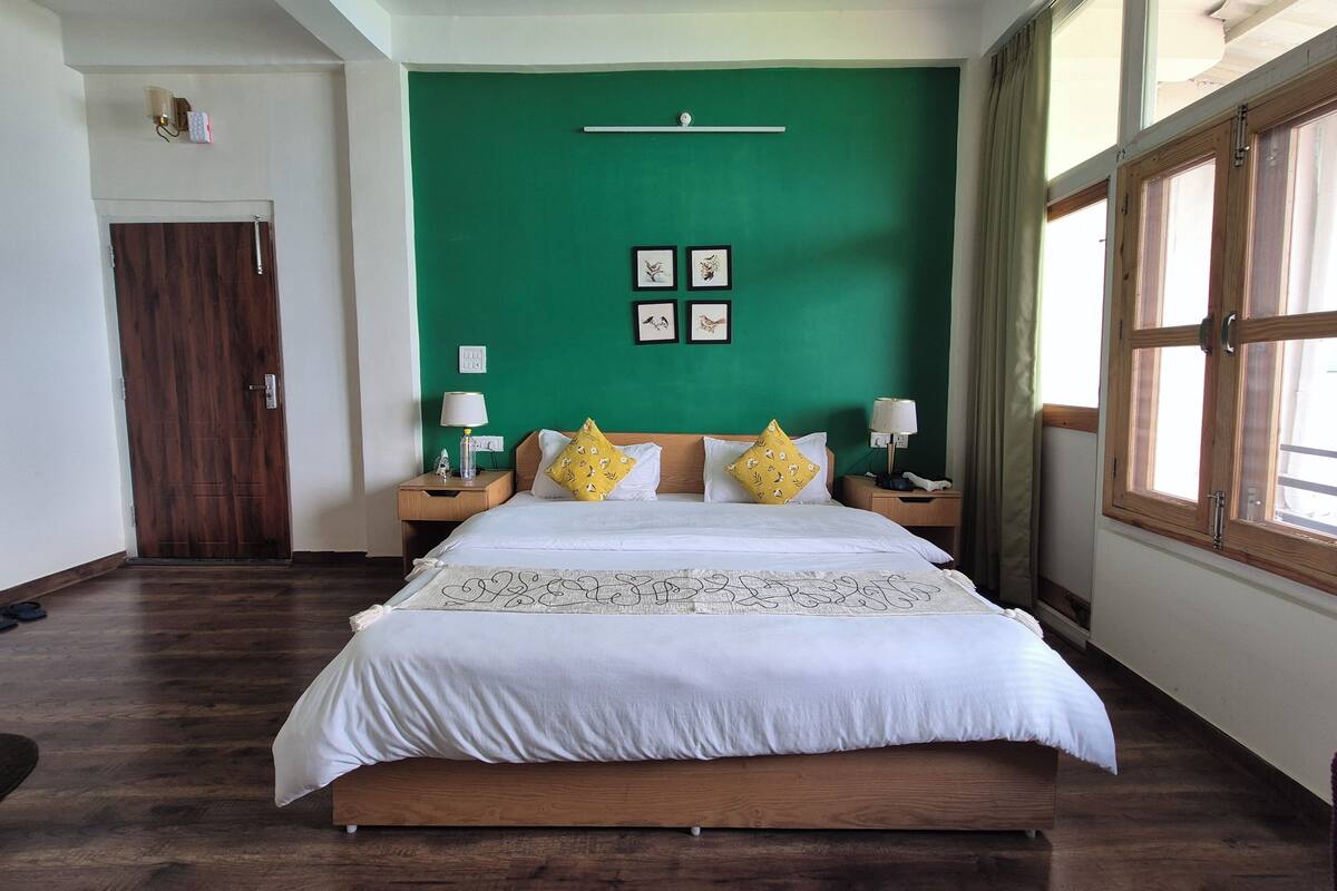 Een hotelkamer met een groene accentmuur, een houten bedframe, wit beddengoed en twee nachtkastjes met lampen.