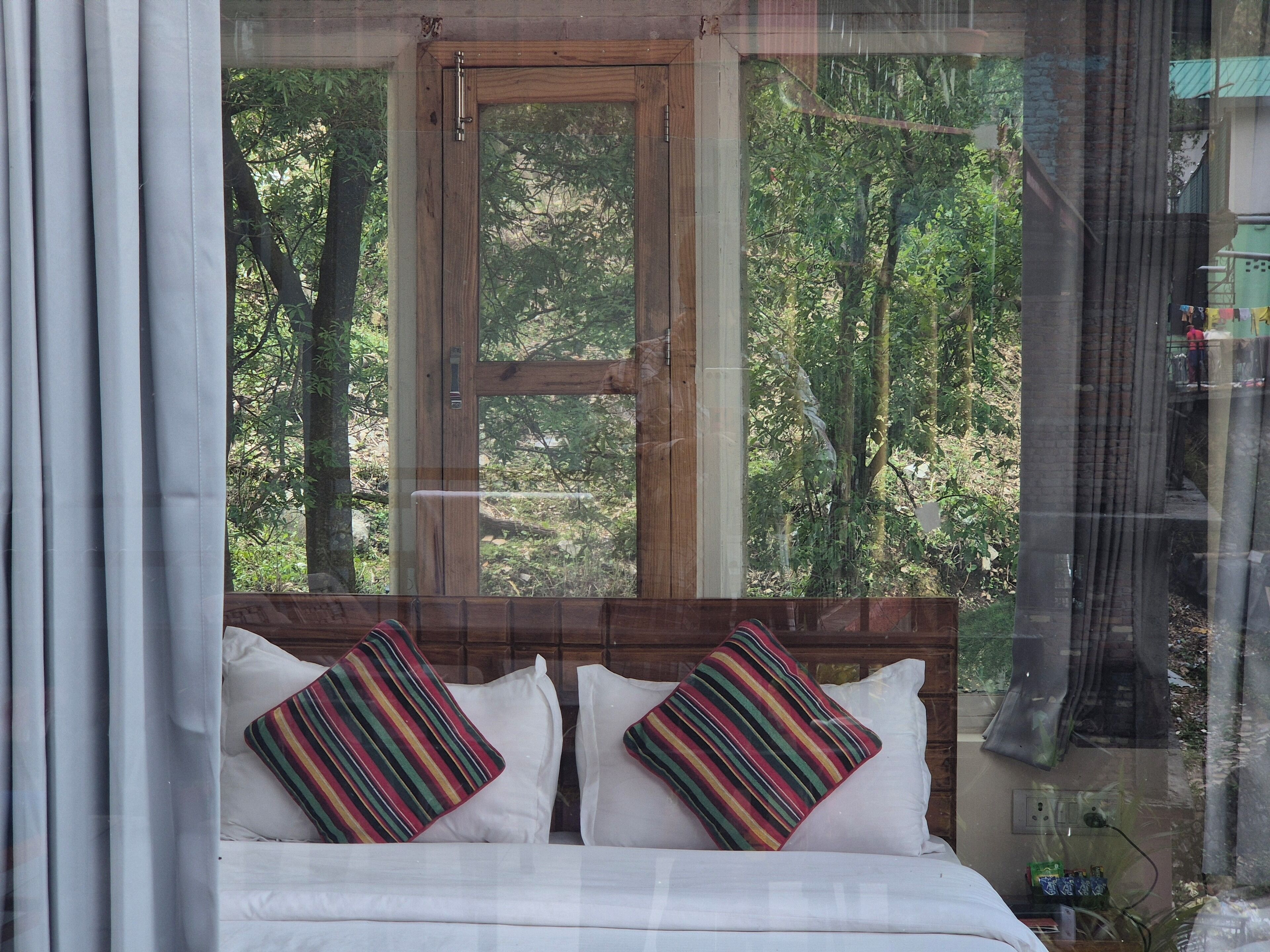 A bedroom with a wooden headboard, two white pillows, and a view of a forest through a window.