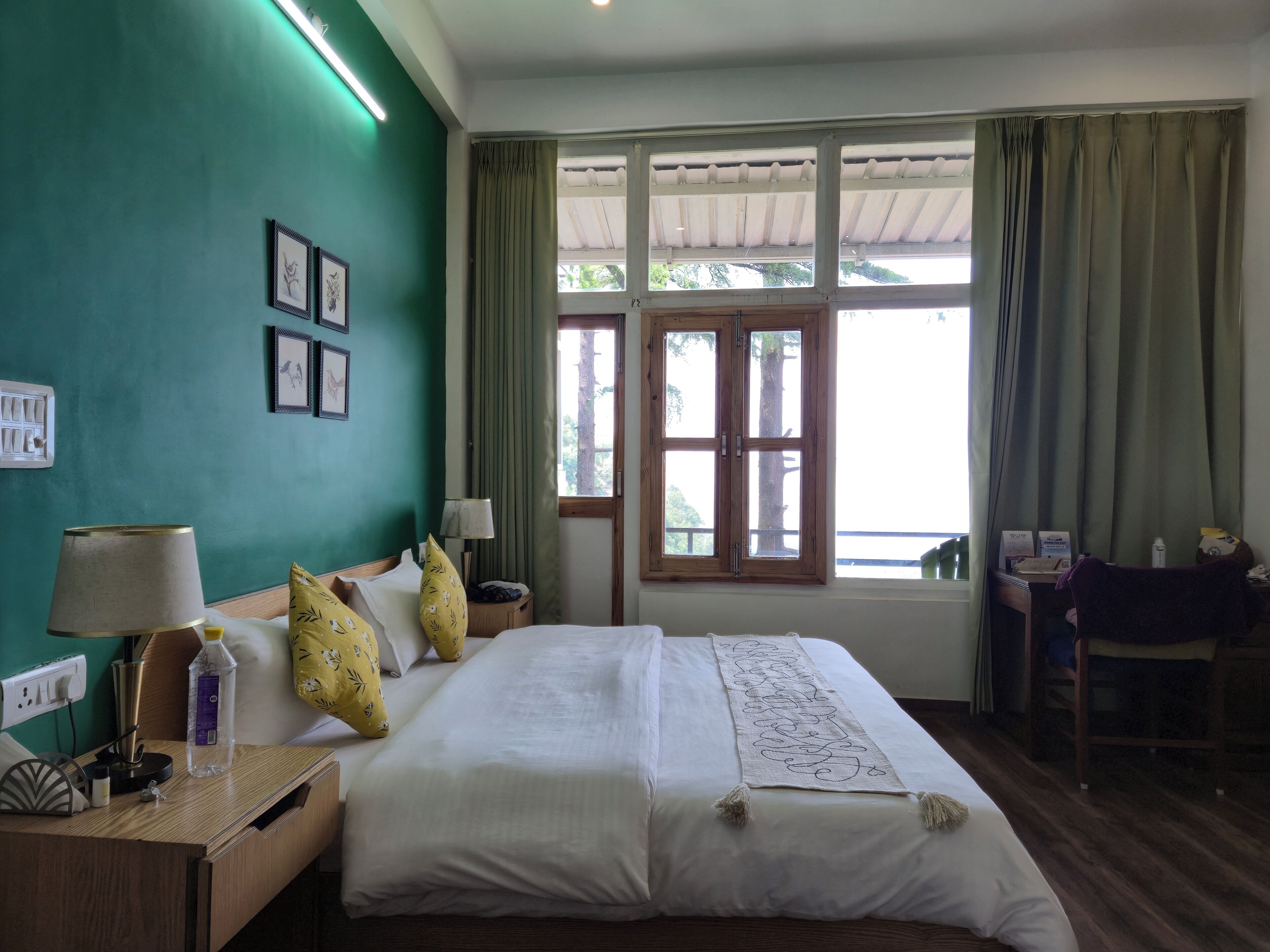 Una habitación de hotel con cama, mesitas de noche, escritorio y ventana con cortinas.