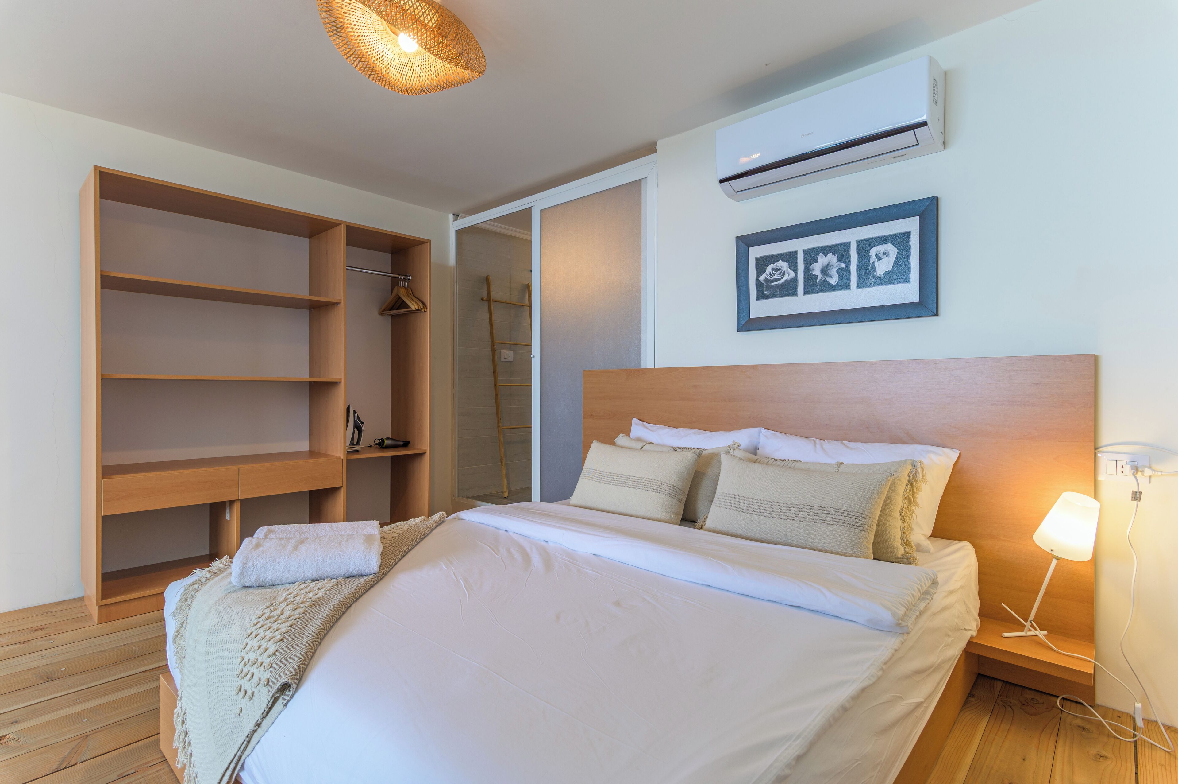 Un dormitorio con cama de madera, mesita de noche con lámpara, armario y aire acondicionado instalado en la pared.