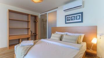 Un dormitorio con cama de madera, mesita de noche con lámpara, armario y aire acondicionado instalado en la pared.