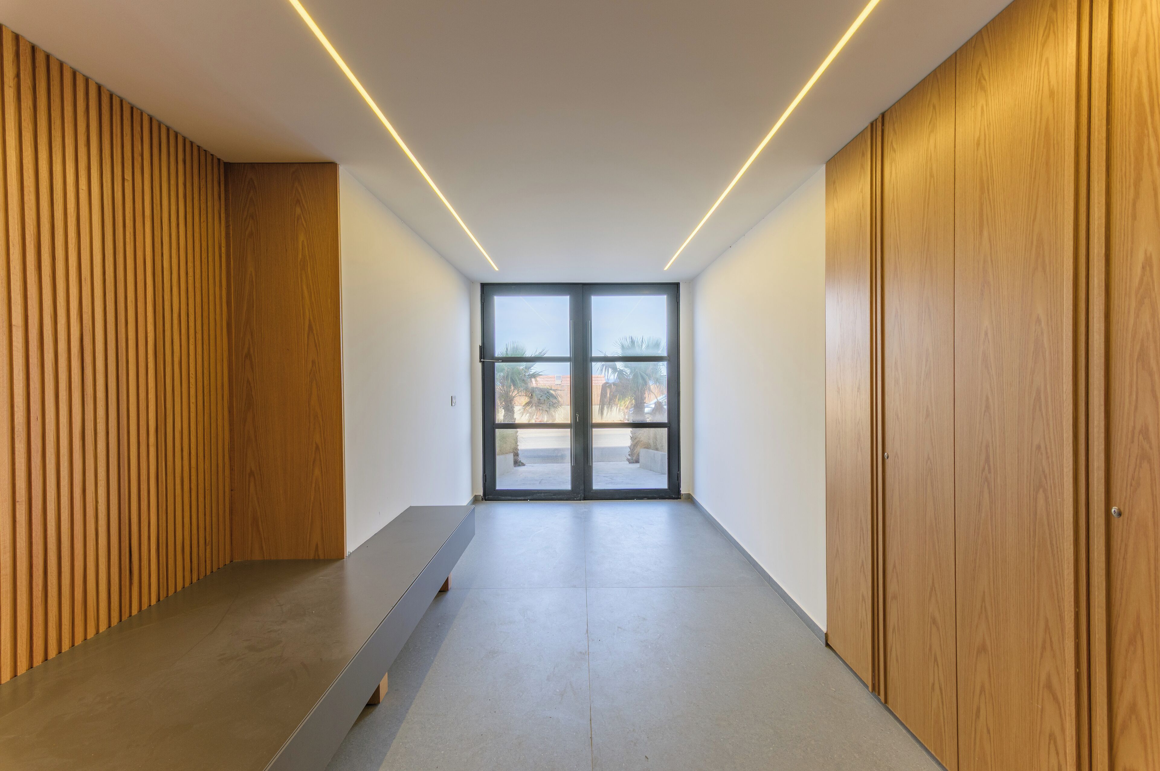 Un corridoio moderno con rivestimenti in legno, una panca e un'ampia porta scorrevole in vetro che dà su uno spazio esterno.