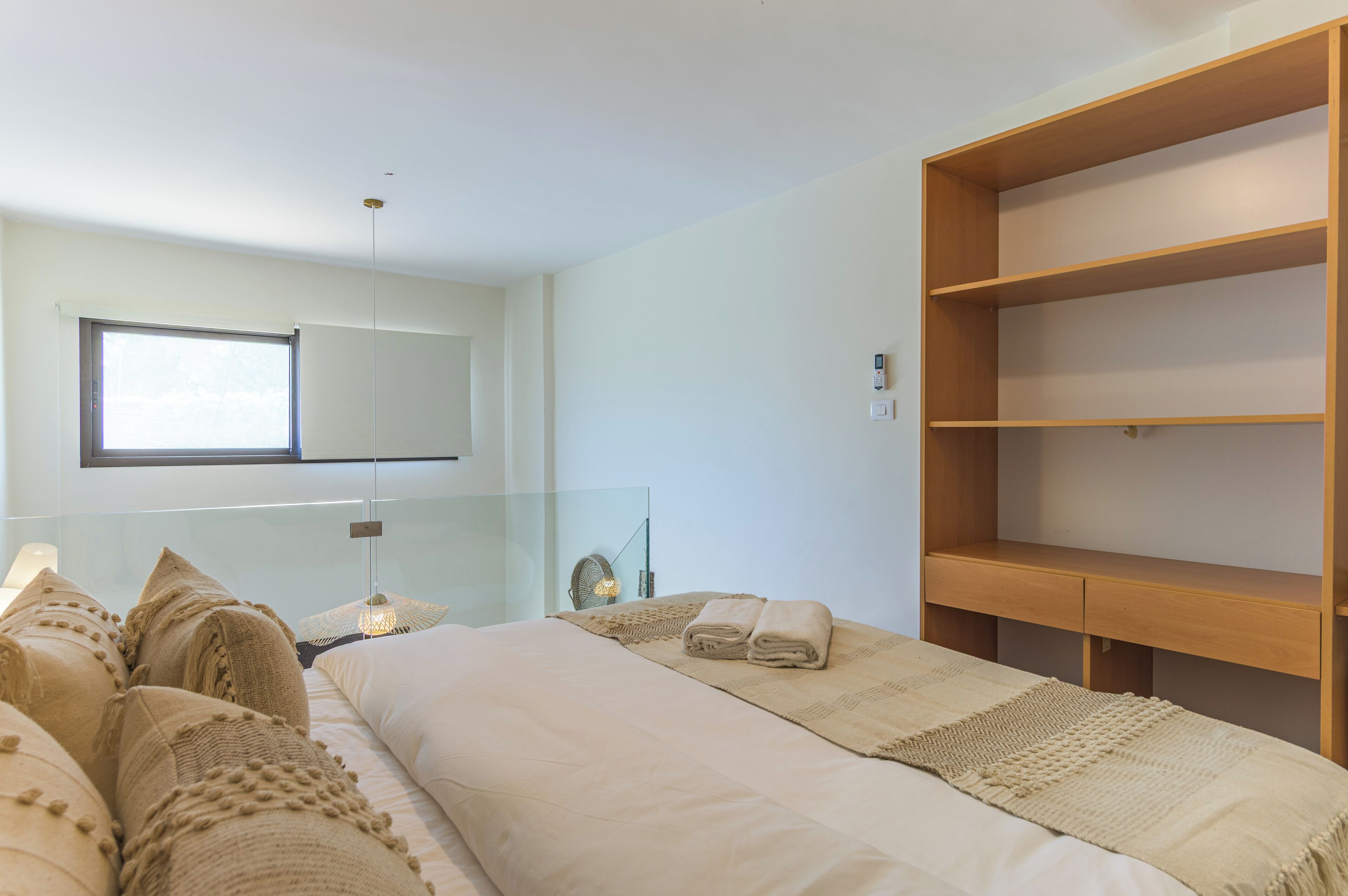 A modern bedroom with a large bed, a glass partition, a wooden shelf unit, and a large window.