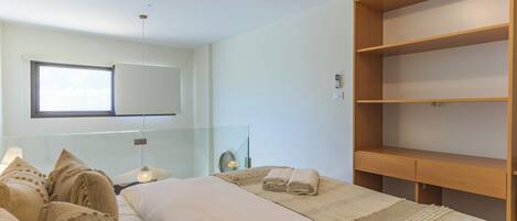 Un dormitorio moderno con una cama grande, un separador de vidrio, una estantería de madera y un ventanal amplio.