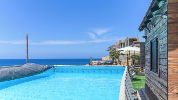 A swimming pool with a view of the sea, wooden buildings, and umbrellas. - Sea Lofts-Kfar Abida Oceanfront Retreats (Batroun)