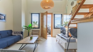 A modern living room with a sofa, coffee table, and TV. There is a staircase with glass railings and a view of the outside. - Sea Lofts-Kfar Abida Oceanfront Retreats (Batroun)