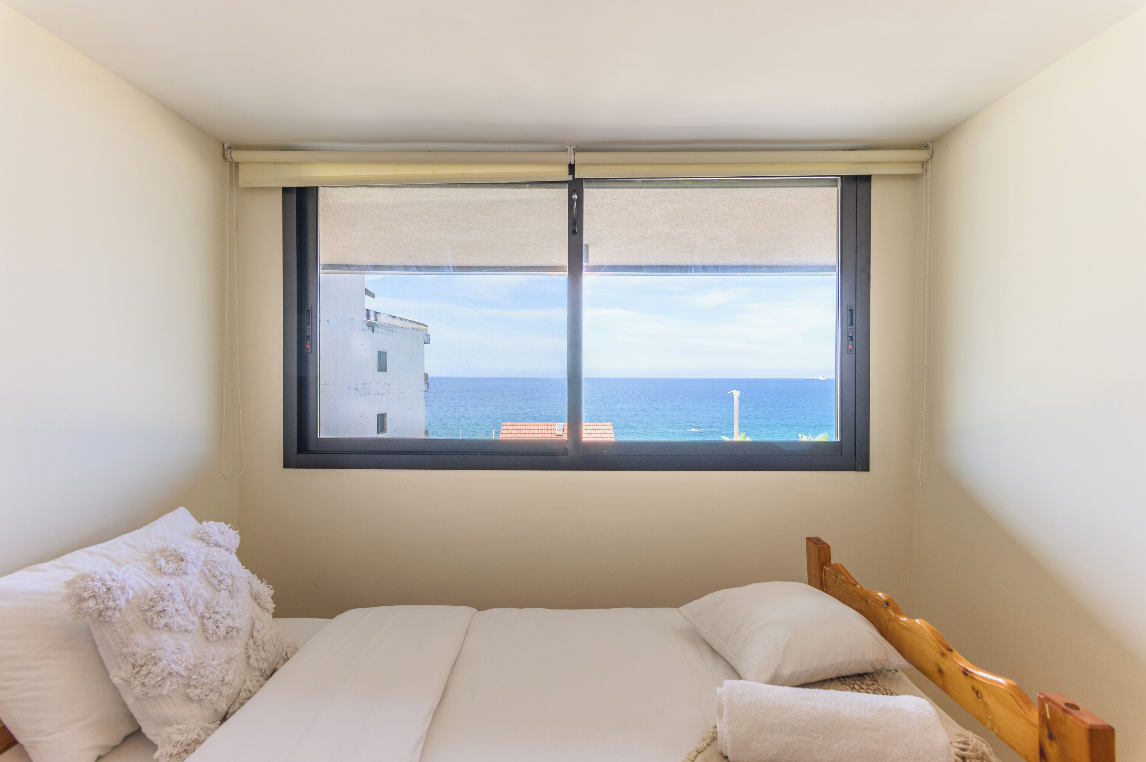 A bedroom with a large window, a bed, and a view of the sea.