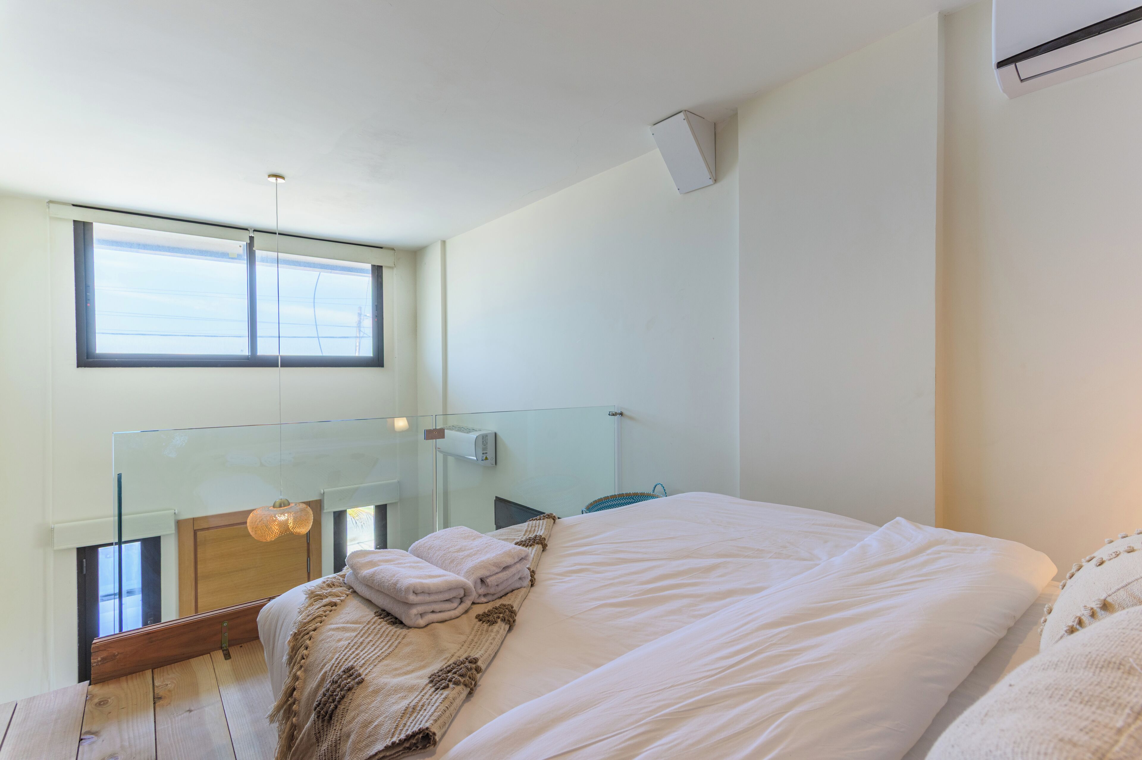 A modern bedroom with a large bed, a glass balcony, and a view of the sky.