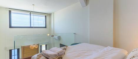 A modern bedroom with a large bed, a glass balcony, and a view of the sky.