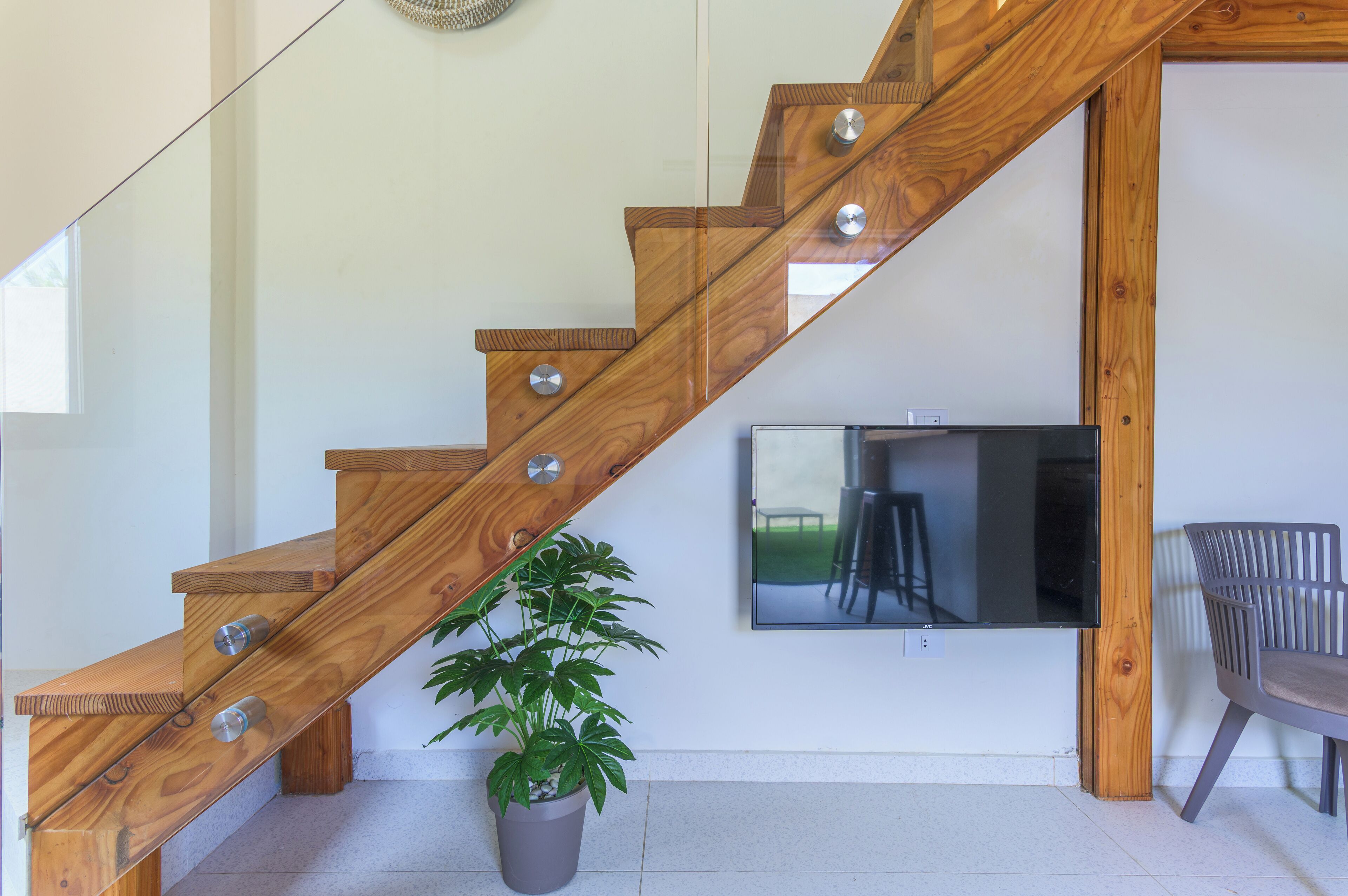 A wooden staircase with a glass railing, a potted plant, and a mounted television.