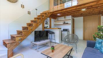 A modern interior with a wooden staircase, a flat-screen TV, a dining table, and a sofa.