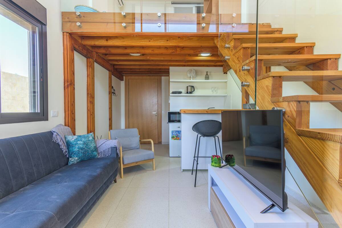 A modern living room with a sofa, a chair, a TV, and a staircase with wooden railings.