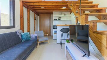 Un salon moderne comprenant un canapé, un fauteuil, un téléviseur et un escalier avec des rampes en bois.