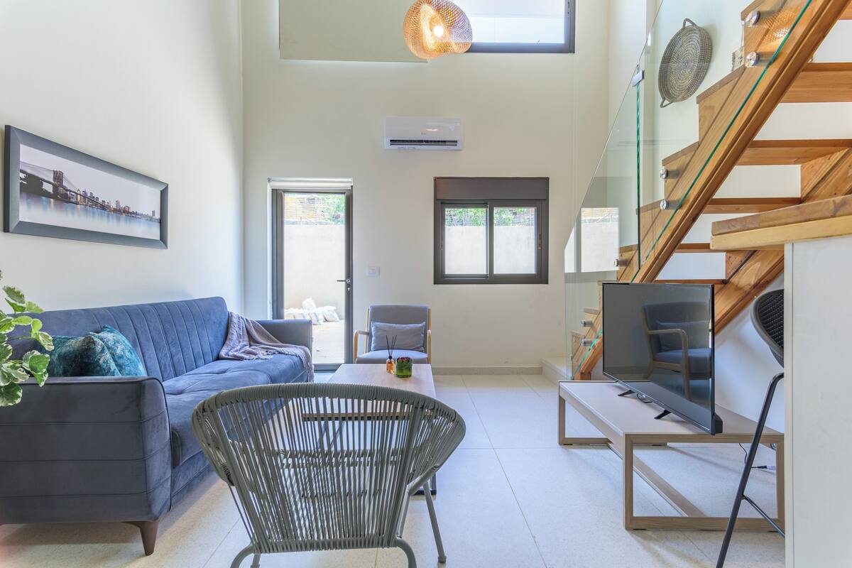 A modern living room with a sofa, a chair, a table, and a staircase.