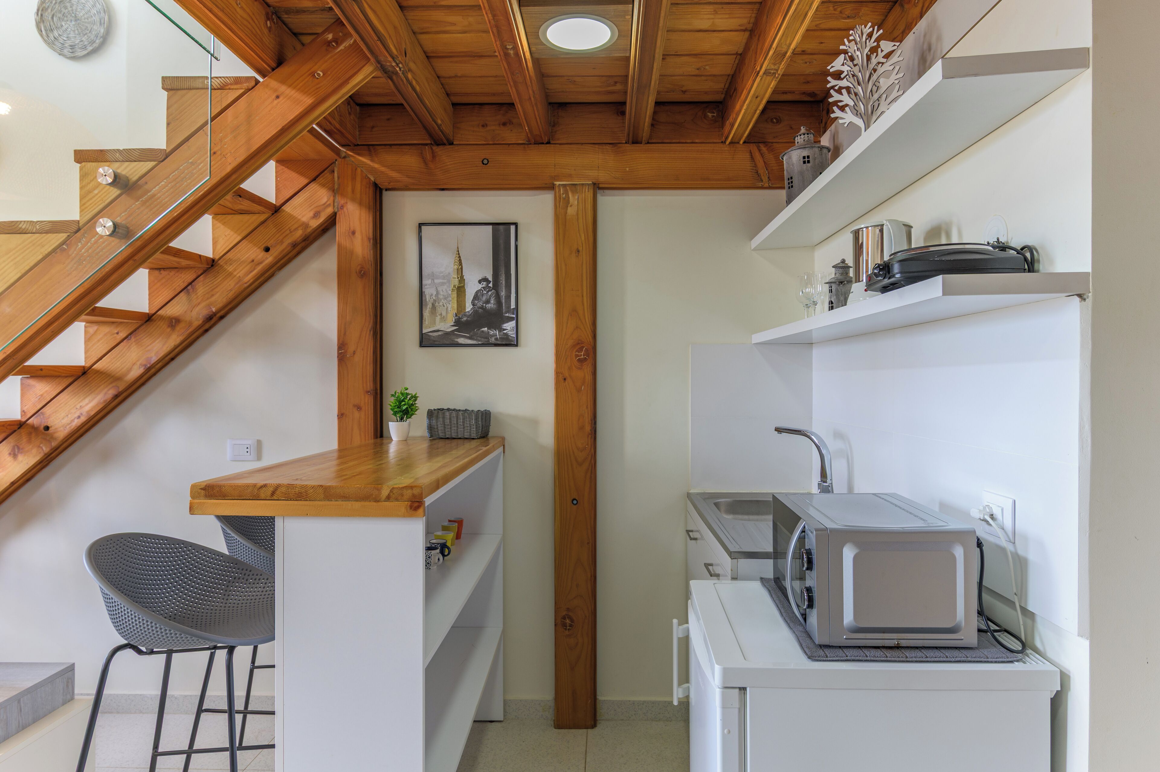 A compact kitchen with a wooden staircase, a small dining area, and a microwave on a white countertop.