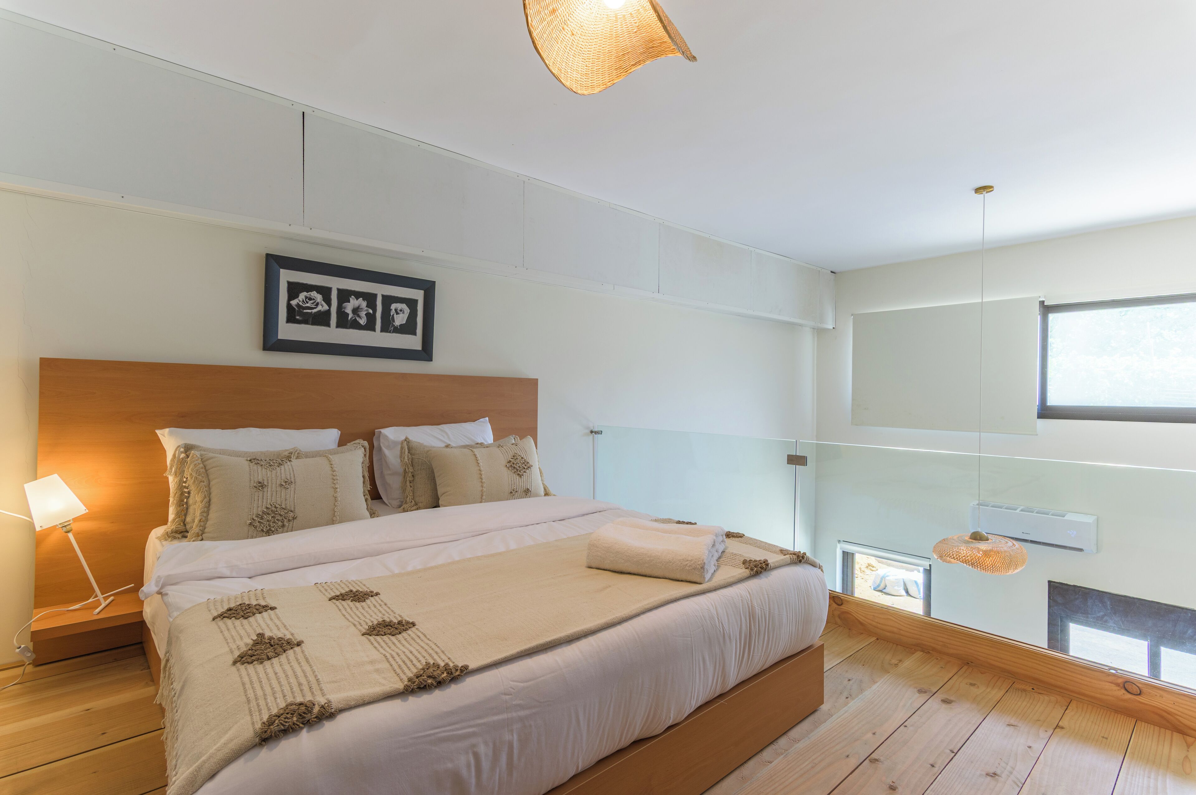 Quarto moderno com uma cama grande, luminária de cabeceira, quadro na parede e janela com vista.