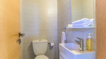 A bathroom with a toilet, a sink with a soap dispenser, and a towel hanging on a rack.
