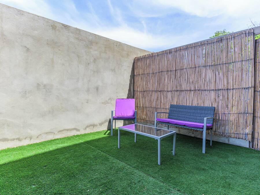 A patio with a concrete wall, a bamboo fence, and two chairs with cushions.